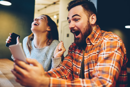 Young man and woman laughing while using their phones