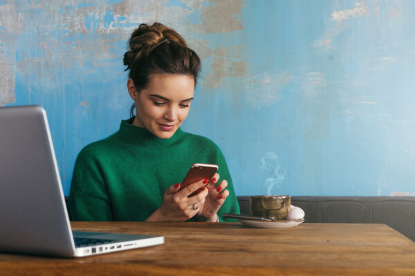 Young woman sitting at table with smartphone and laptop