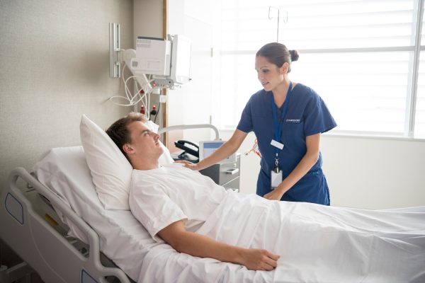 Female nurse tending to male patient in hospital bed